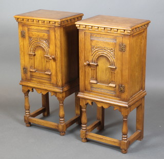 A pair of carved oak bedside cabinets with moulded dentil cornices, enclosed by arch panelled doors, raised on turned and block supports 37" x 16 1/2" x 12" 