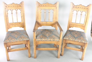 A set of 12 oak Gothic style high back dining chairs with arcaded backs and upholstered seats, raised on turned and block supports, comprising 8 carvers and 4 standard