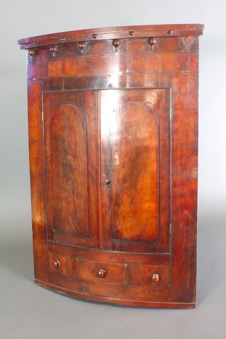 A Georgian mahogany bow front hanging corner cabinet the upper section with moulded and shaped cornice, fitted shelves enclosed by arched panelled doors, the base fitted 1 long drawer flanked by 2 dummy drawers 48"h x 34 1/2"w x 18"d 

