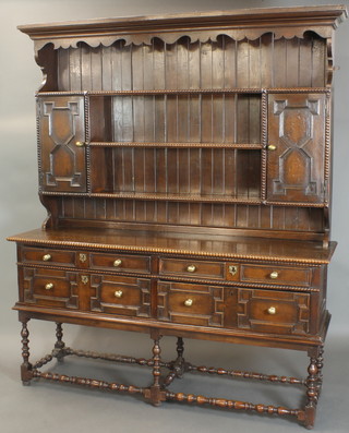 A Jacobean style Continental oak dresser, the raised back with geometric mouldings and cornice above 3 shelves flanked by a pair of cupboards above 4 long drawers with brass handles and iron locks, raised on spiral turned and block supports 87"h x 73"w x 21"d 