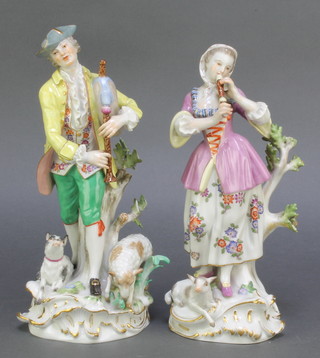 A pair of early 20th Century Meissen figures of a pair of musicians, the gentleman with a dog and sheep at his feet, the lady with a lamb at her feet on raised rococo bases 9" and 10"  