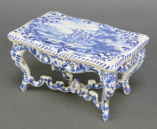 A Delft model of a rectangular dining table, the top decorated with figures in an extensive country landscape, the legs decorated with scrolls 6" 