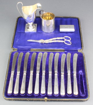 A silver helmet shaped cream jug Birmingham 1910, a pair of silver plated grape scissors, snuff box and mug together with a cased set of 11 (x12) butter knives 