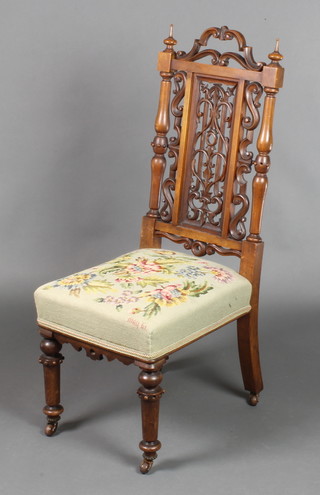 A Victorian carved and pierced walnut nursing chair with pierced panel to the back and 2 turned columns to the side, having a Berlin wool work upholstered seat on turned supports 