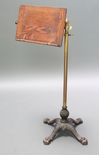 A Victorian oak brass and iron reading stand with rectangular panel, raised on an adjustable stand and having iron paw feet 36"h rising to 53"h 