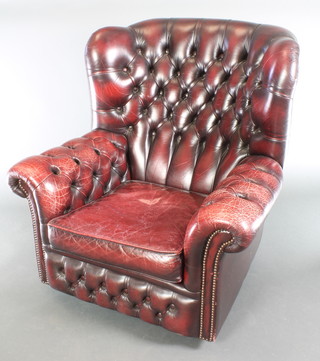 A winged armchair upholstered in claret red buttoned back leather 