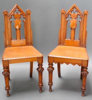 A pair of Victorian light oak Gothic style hall chairs with pierced backs and solid seats, raised on turned supports