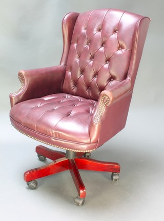 A winged revolving office chair upholstered in burgundy buttoned rexine