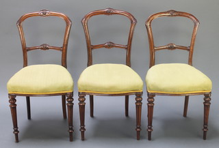 A set of 3 Victorian carved walnut balloon back chairs with mid rails and upholstered seats, raised on turned and fluted supports 