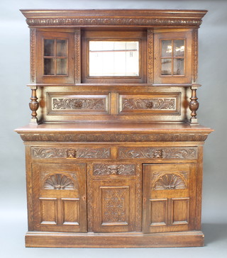 A Victorian carved light oak sideboard, the raised back fitted a rectangular bevelled plate mirror flanked by a pair of cupboards enclosed by glazed panelled doors above a recess, the base fitted 2 long and  1 short drawers with triple cupboard beneath 76"h x 60"w x 22 1/2"d 