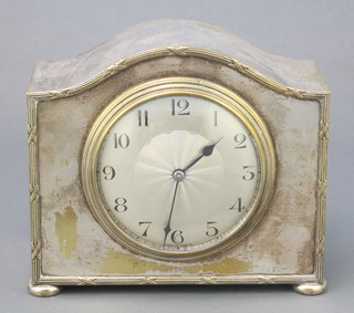 A 1930's bedroom timepiece with silvered dial and Arabic numerals contained in an arched silver plated case, raised on bun feet 