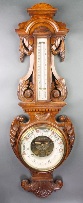 A Victorian aneroid barometer and thermometer contained in a carved oak wheel case