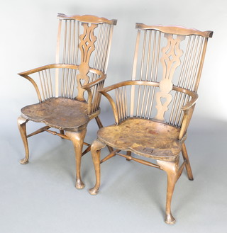A pair of figured elm stick and rail back carver chairs with saddle seats, raised on cabriole supports with H framed stretcher