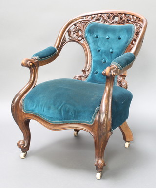 A Victorian pierced and carved mahogany show frame open arm chair upholstered in blue buttoned material, raised on cabriole supports 