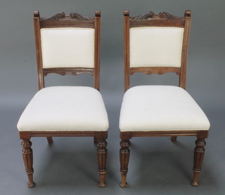 A pair of Victorian carved walnut dining chairs with scroll decoration to the top, with upholstered seats and backs, raised on turned and fluted supports 