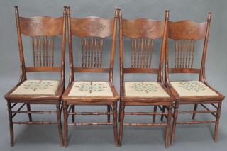 A set of 4 late Victorian carved oak stick and rail back dining chairs with upholstered seats, raised on turned supports