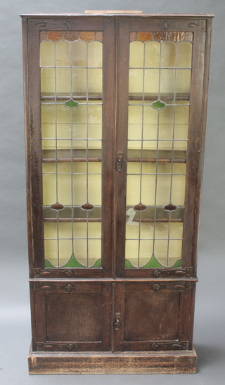 An Art Nouveau oak display cabinet fitted adjustable shelves enclosed by lead glazed panelled doors with embossed metal hinges, the base fitted a cupboard enclosed by panelled doors 73"h x 35"w x 11 1/2"d 