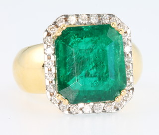 An 18ct yellow gold emerald and diamond ring, the centre emerald cut stone approx 6.77ct surrounded by brilliant cut diamonds, approx. 0.95ct, size Q 1/2