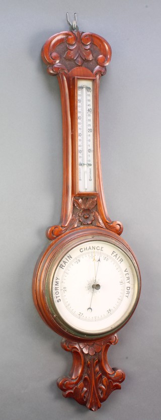 An Edwardian aneroid barometer and thermometer with porcelain dial contained in a carved walnut wheel case 