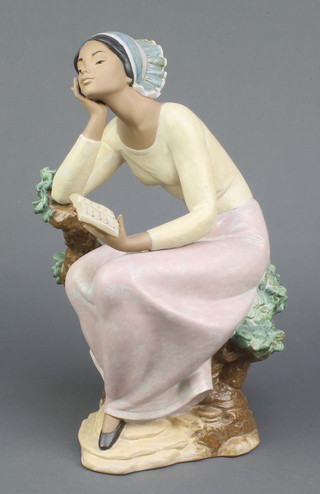 A matt glazed Lladro figure of a lady holding a book and leaning on a stump 13" 