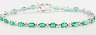 An 18ct white gold emerald and diamond line bracelet with 24 oval cut emeralds interspersed with brilliant cut diamonds, emeralds 5.21ct, diamonds 0.32ct 