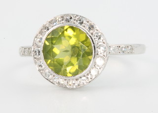 An 18ct white gold peridot and diamond cluster ring, the centre stone enclosed by 16 brilliant cut diamonds with 3 diamonds to each shoulder, size N 1/2