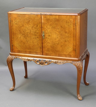 A  Queen Anne style figured walnut cocktail cabinet with fitted interior, enclosed by panelled doors  with cross banded decoration, having a carved and pierced apron and raised on cabriole supports 40"h x 35"w x 17"d 
