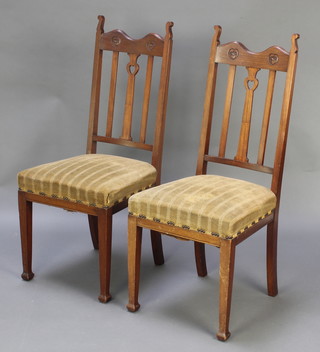 A pair of mahogany Art Nouveau stick and rail back dining chairs with upholstered seats, raised on square tapering supports 