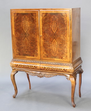 A Continental figured walnut cocktail cabinet on stand with quarter veneered top and panelled doors with crossbanding, the mirrored back interior fitted niche shelves and drawers, the base fitted 2 long drawers raised on carved cabriole supports  58 1/2"h x 39 1/2"w x 17 1/2" 