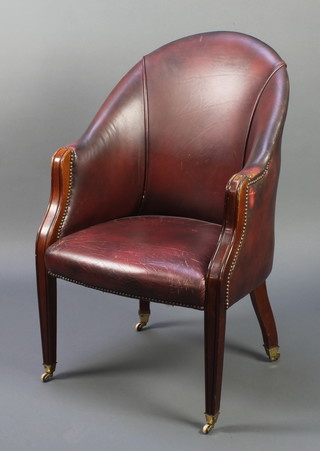 A Georgian style mahogany tub back chair upholstered in red leather material, raised on square tapering supports, brass caps and casters 