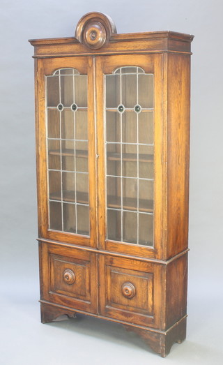 An Art Nouveau oak bookcase with arched top, fitted adjustable shelves enclosed by lead glazed panelled doors above a cupboard enclosed by panelled doors 79"h x 37 1/2"w x 11"d 