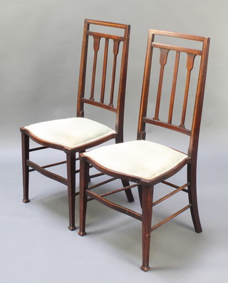 A pair of Edwardian Art Nouveau inlaid mahogany stick and rail back bedroom chairs with shaped seats raised on square tapered supports 