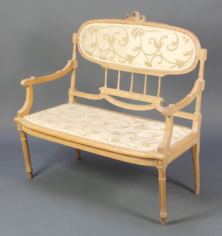 A French style carved light oak double chair back settee, raised on turned and reeded supports
