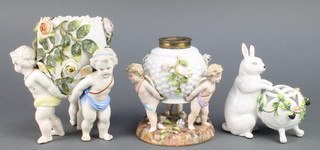A 19th Century German porcelain oil lamp base supported by 3 cherubs with applied flowers 6", a ditto bowl supported by 3 cherubs 7" and a vase with a seated rabbit 6" 