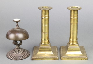 A Victorian iron table bell 5" with push button (cracked) and a pair of 19th Century brass candlesticks on square feet 6" 
