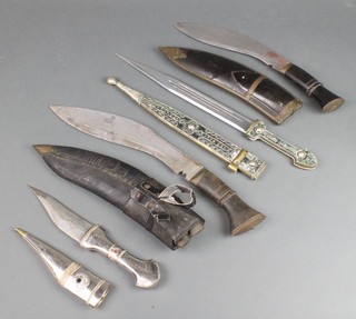 A Kukri with 11" blade complete with 2 skinning knives and leather scabbard, a Kukri with 9" blade and horn grip and scabbard, an Eastern dagger with 5" blade, white metal grip and scabbard together with 1 other Eastern dagger with double edge blade 11"  