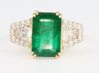 An 18ct yellow gold emerald and diamond ring, the centre stone approx. 3.2ct surrounded by baguettes approx. 0.24ct and brilliants 0.22ct, size L 1/2