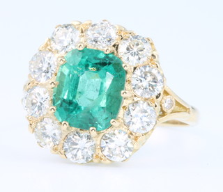 A yellow gold emerald and diamond cluster ring, the centre cushion cut stone approx. 2.8ct surrounded by 10 brilliant cut diamonds approx. 2ct, size O