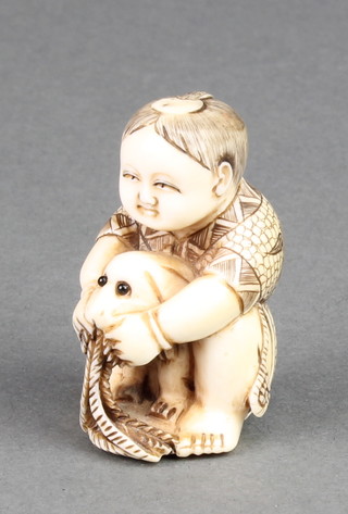 A carved ivory Netsuke in the form of a child with a puppy between his legs, signed 1 3/4" 