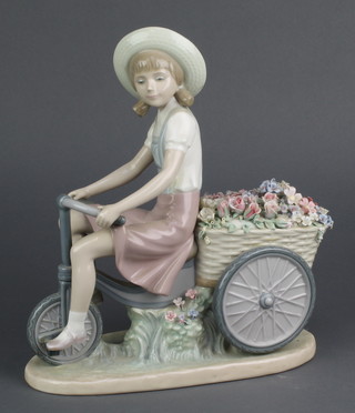 A Lladro figure of a girl riding a tricycle pulling a basket of flowers 10" 