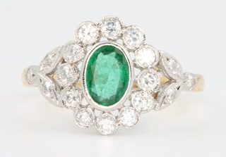 An 18ct yellow gold emerald and diamond Edwardian style ring, the centre stone approx 0.6ct surrounded by brilliant cut diamonds approx. 0.85ct size R