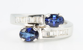 A 14ct white gold sapphire and diamond crossover ring, the 2 oval sapphires approx 1.3ct flanked by tapered baguette diamonds approx 0.3ct size K 