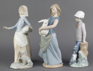 A Nao figure of a boy leaning on a tree trunk with a dog at his feet 9", a ditto of a girl carrying a basket with a dog at her feet 10 1/2" and 1 other of a girl holding a white rabbit 9" 