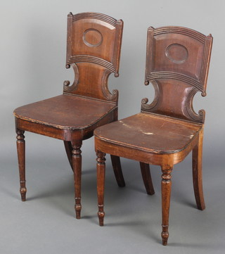 A pair of Georgian mahogany hall chairs with shaped backs and solid seats, raised on turned supports 