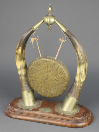 A brass dinner gong with horn supports raised on a carved oak base 19" x 15 1/2" x 7"