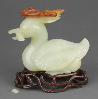 A 20th Century Chinese carved jade figure of a duck holding a lotus leaf between its beak 5", raised on a carved wooden stand 