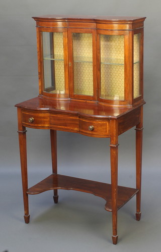 An Edwardian inlaid mahogany cabinet of serpentine outline, fitted a shelf enclosed by bevelled glazed panelled door, the base fitted a drawer with undertier, raised on square tapered supports, spade feet 45"h x 24"w x 14"d 
