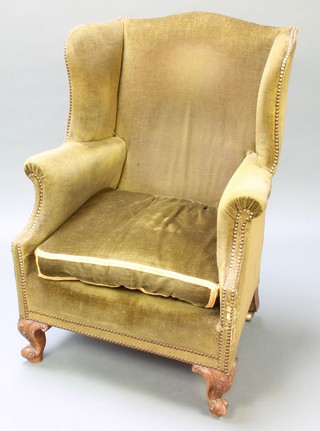 A 19th Century Continental winged armchair upholstered in green material, raised on carved cabriole supports 