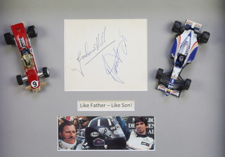 Graham Hill and Damon Hill, a rectangular white paper signed and mounted in a frame inscribed "Like Father Like Son" with 2 model racing cars 11" x 13 1/2" NB, Graham Hill's signature was obtained by the vendor at Goodwood in 1957 and Damon Hill's in 1998 