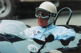 A coloured photograph of Sir Stirling Moss sat in a racing car, signed 6" x 9 1/2" 